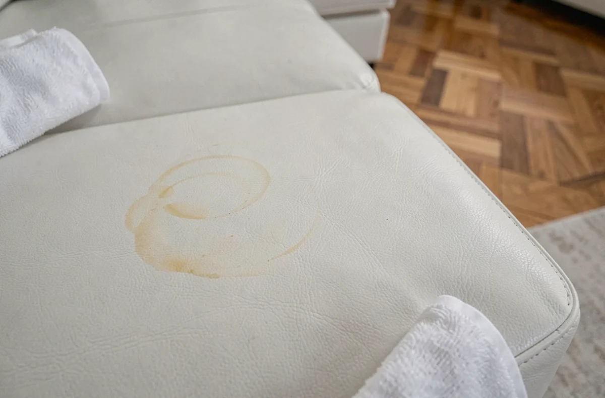 Gros plan sur un canapé en cuir blanc montrant une trace jaune et une auréole comparées à une zone nettoyée